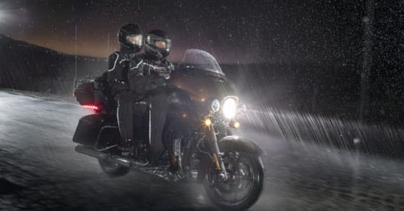 Two people riding a motorcycle in the dark and in the rain